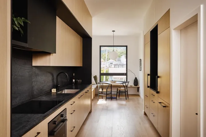Contemporary kitchen featuring light wood-finish cabinetry and matte black countertops with a matching backsplash