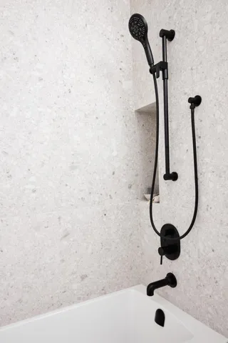 White bathtub featuring a wall-mounted matte black tub filler and shower system