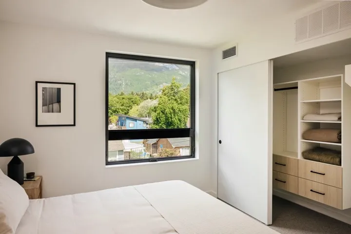 Bedroom featuring a large black-framed window, built-in closet organization system, two lower drawers with black hardware, and a white sliding door
