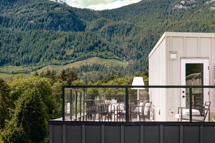 Rooftop deck featuring glass railings, a white exterior wall with a door, and a mountainous, tree-lined backdrop