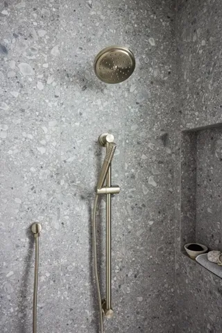 Shower with terrazzo-style wall tile, a rain shower head, handheld shower fixture, and a built-in niche with a floating shelf