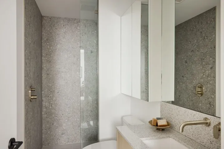 Bathroom featuring a glass-enclosed shower with full-height stone-finish tile, a light wood-finish vanity, and a wall-mounted faucet