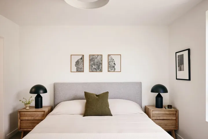 Bedroom featuring a neutral color palette, ceiling-mounted light fixture, light wood-finish nightstands with drawers, and a textured fabric headboard