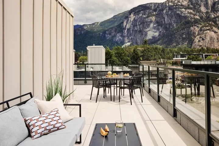 Expansive rooftop terrace featuring light-colored paving, a glass and metal railing, and a mountain backdrop
