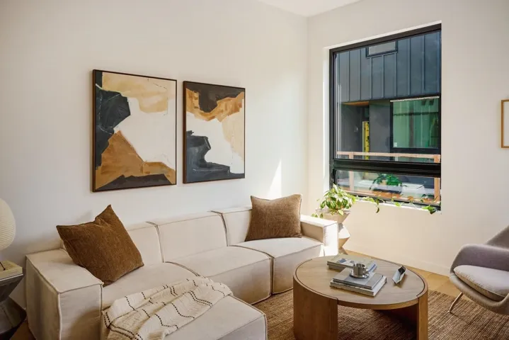 Bright living area featuring a large black-framed window, light wood-finish flooring, and white walls