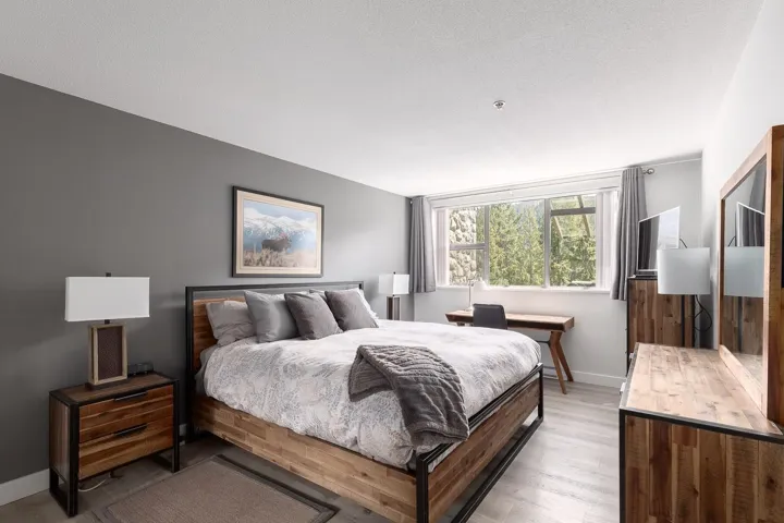 Spacious bedroom featuring light wood-finish flooring, a full-wall window with exterior scenery, a built-in desk, and a neutral color palette