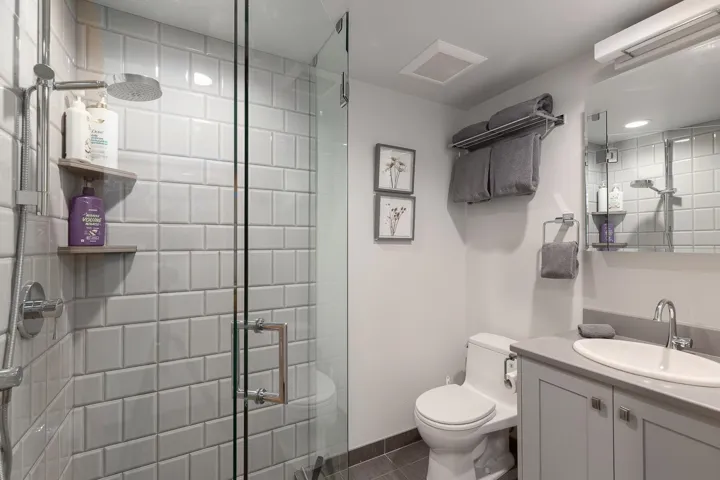 Contemporary bathroom featuring a glass-enclosed shower with subway tile surround, a rain showerhead, a single vanity with an integrated sink and light grey cabinetry, and dark grey tile flooring