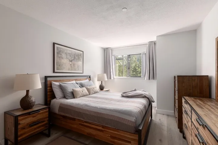 Bedroom featuring light-toned walls, a window with outdoor tree scenery, and wood-finish flooring