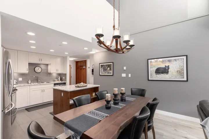 Vaulted ceiling dining area featuring a live-edge wood dining table, an open-concept kitchen with light cabinetry, stainless steel appliances, and a kitchen island with seating