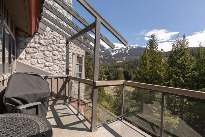Outdoor balcony featuring a stone facade, glass panel railing, and a slatted overhead structure