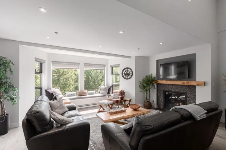 Spacious living area featuring a bay window with built-in bench seating, wood-finish flooring, recessed lighting, and a fireplace with a wood mantle and stone surround