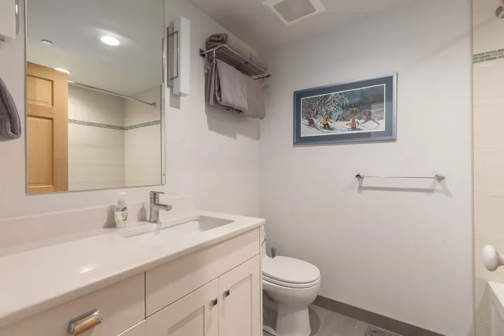 Bathroom featuring a white vanity with an integrated sink and chrome faucet, a rectangular mirror, and a toilet with a ceramic tile floor