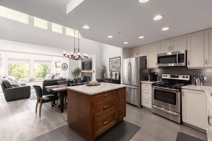 Open-concept kitchen featuring stainless steel appliances, granite countertops, a wood-finish island, and recessed lighting