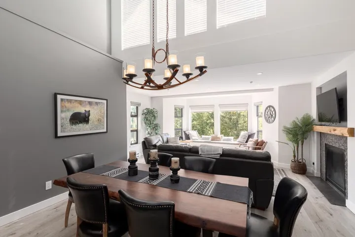 Dining area featuring a vaulted ceiling with clerestory windows, a multi-arm chandelier, wood-finish flooring, and a fireplace with a stone surround and wood mantel