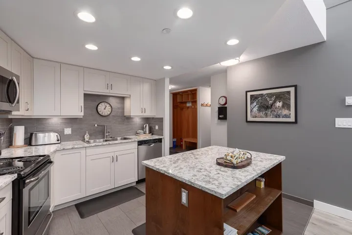 Kitchen featuring white shaker-style cabinetry, a stone countertop, and a gray tile backsplash