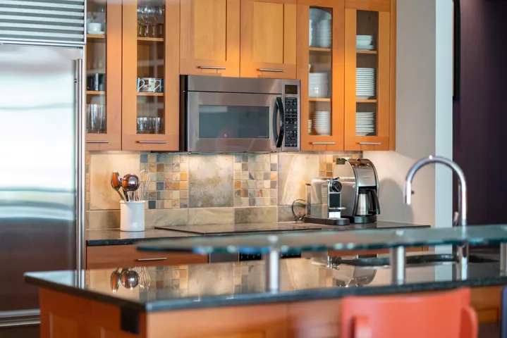 Kitchen with appliances with stainless steel finishes, decorative backsplash, brown cabinetry, and glass insert cabinets