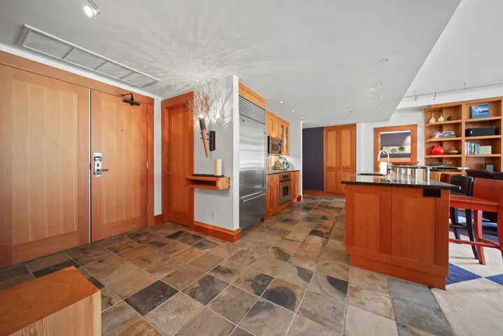 Kitchen with appliances with stainless steel finishes, dark countertops, dark stone finish floors, a kitchen bar, and an island with sink