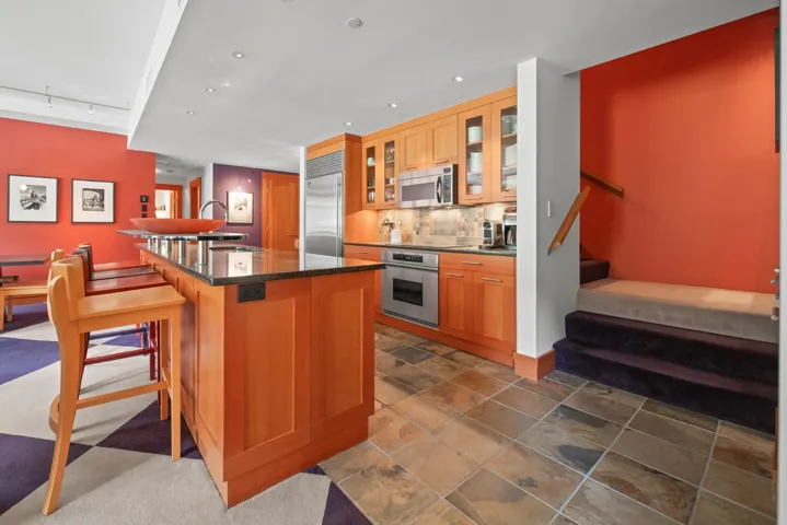 Kitchen with appliances with stainless steel finishes, a kitchen island, a kitchen bar, glass insert cabinets, and track lighting