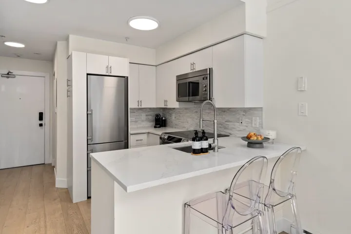 Kitchen with a kitchen breakfast bar, backsplash, stainless steel appliances, a peninsula, and white cabinets