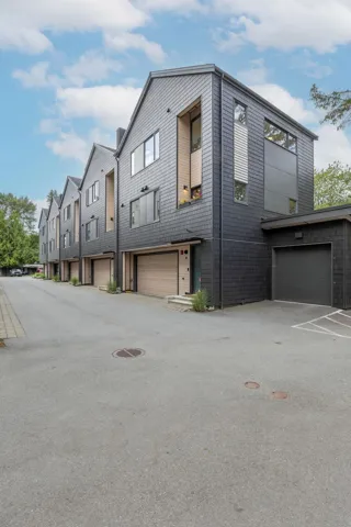 Contemporary townhome exterior featuring dark grey shingle siding, a prominent gabled roofline, and varied window placements