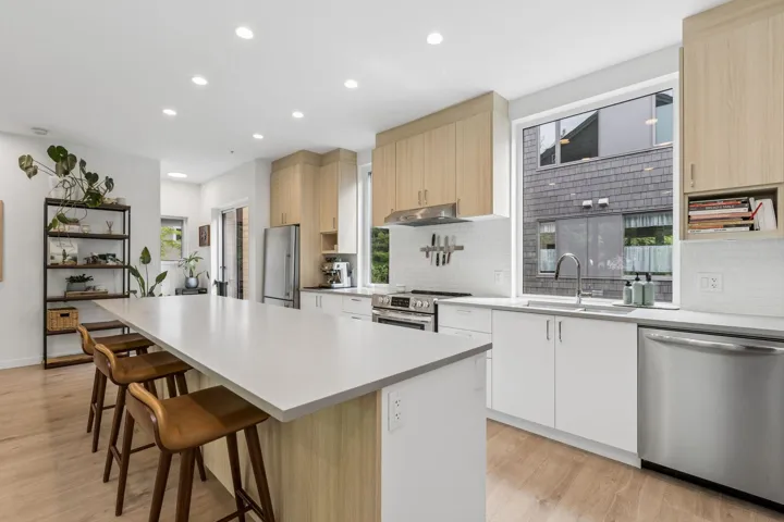 Modern kitchen featuring a large island with seating, stainless steel appliances, light wood-finish cabinetry, white subway tile backsplash, and recessed lighting