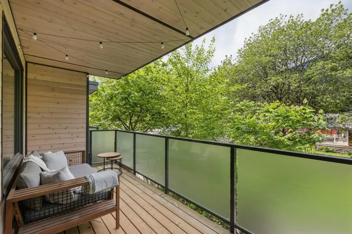 Covered outdoor balcony featuring wood-finish siding, wood-finish flooring, and a frosted glass panel railing