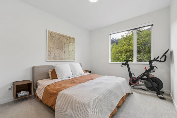 Bright room featuring a window overlooking natural scenery, neutral carpeting, a light-toned upholstered headboard, and a built-in floating nightstand