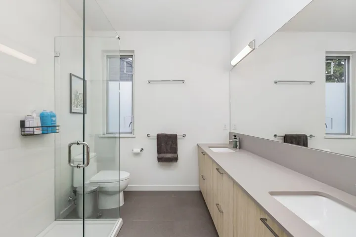 Contemporary bathroom featuring a glass-enclosed shower with white tiled walls, a dual vanity with light wood-finish cabinetry, and a large wall-mounted mirror
