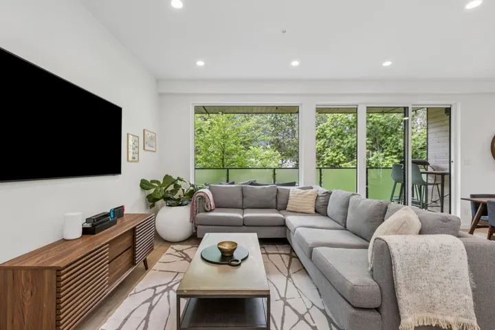Spacious living area featuring light wood-finish flooring, recessed lighting, and a contemporary media console with slatted doors
