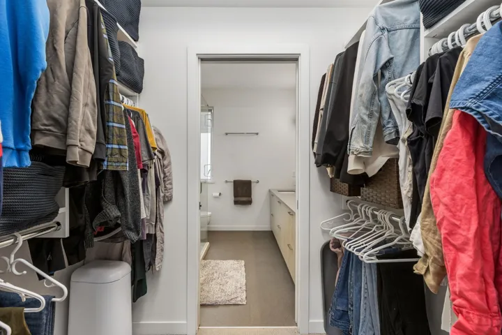 Walk-in closet with built-in shelving, hanging rods, and an entryway to a bathroom featuring a window and an extended vanity