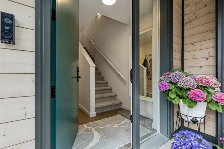 Entryway featuring a deep teal door, light wood-finish siding, and a carpeted staircase with white railings