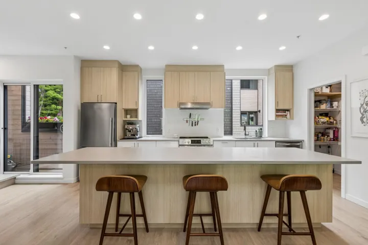Kitchen featuring a large central island with seating, light wood-finish cabinetry, stainless steel appliances, and wood-finish flooring