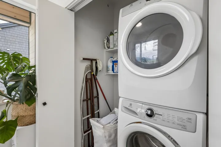 Dedicated laundry area featuring a white stacked washer and dryer unit, integrated shelving, and a bright window