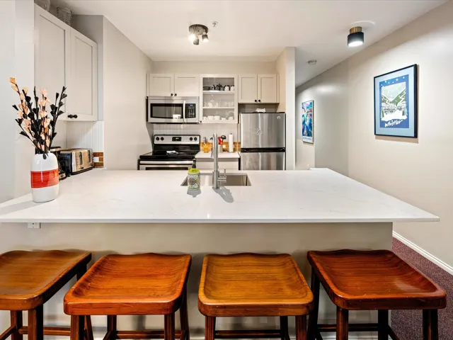 Kitchen featuring a peninsula, stainless steel appliances, light stone countertops, decorative backsplash, and a breakfast bar area