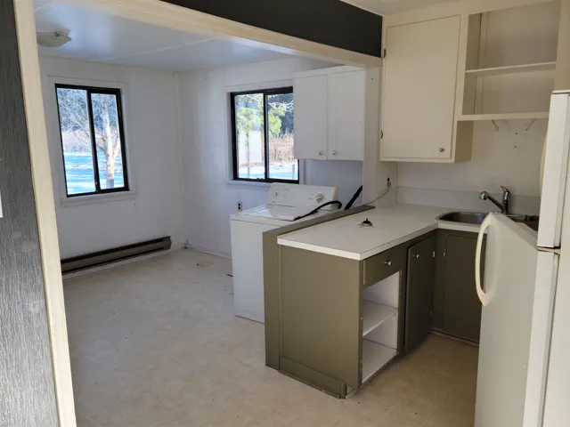 Kitchen featuring washer / clothes dryer, white appliances, cream cabinets, under cabinet range hood, and light floors