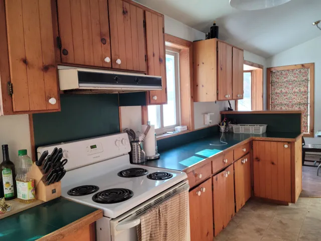 Kitchen featuring white electric stove, extractor fan, brown cabinets, vaulted ceiling, and dark countertops