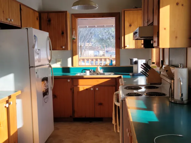 Kitchen with stainless steel range with electric stovetop, freestanding refrigerator, extractor fan, brown cabinetry, and light countertops