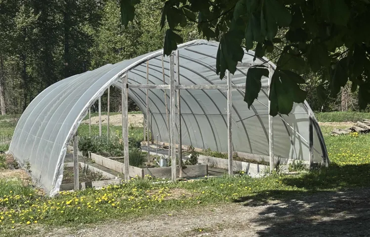 View of vehicle parking with a greenhouse and a garden