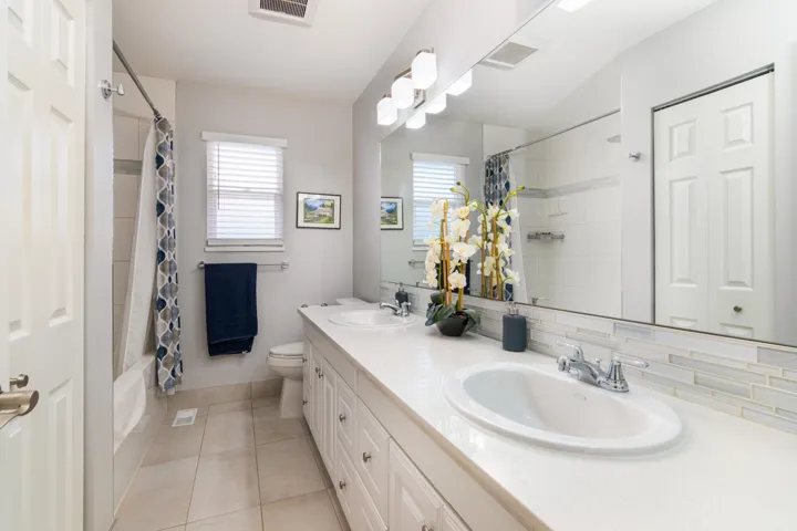 Bathroom with tile patterned flooring, double vanity, shower / bath combo, toilet, and baseboards