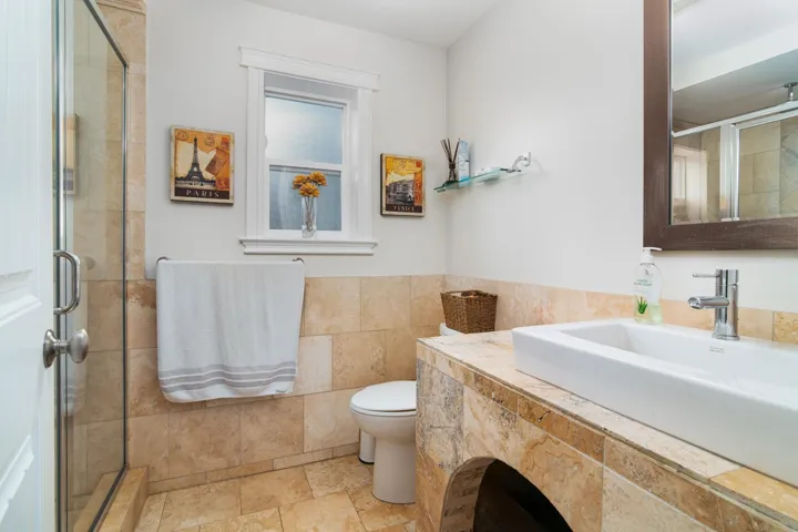 Full bathroom featuring a shower stall, toilet, tile walls, vanity, and wainscoting