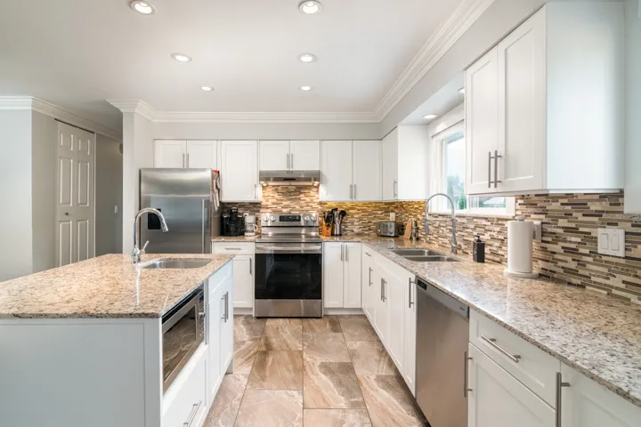Kitchen with appliances with stainless steel finishes, a sink, under cabinet range hood, backsplash, and crown molding