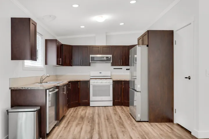 Kitchen featuring appliances with stainless steel finishes, a sink, light wood finished floors, ornamental molding, and dark brown cabinets