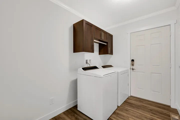 Laundry area featuring cabinet space, ornamental molding, independent washer and dryer, wood finished floors, and baseboards