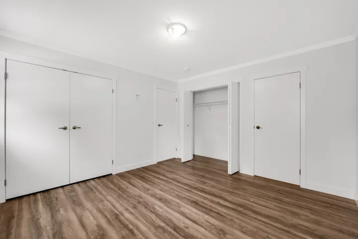Unfurnished bedroom featuring two closets, crown molding, wood finished floors, and baseboards