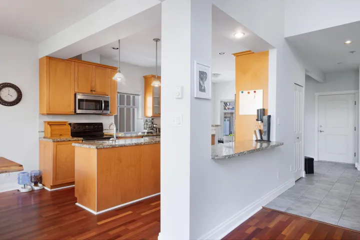 Kitchen featuring stainless steel microwave, black range with electric cooktop, wood finished floors, light stone counters, and baseboards