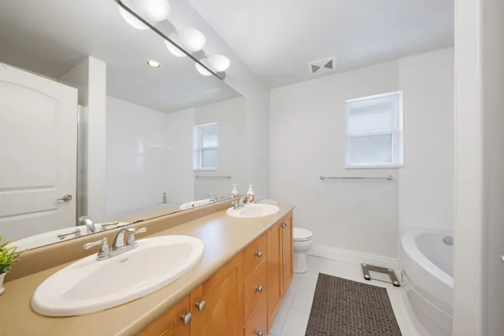 Bathroom featuring double vanity, a tub to relax in, tile patterned floors, baseboards, and toilet