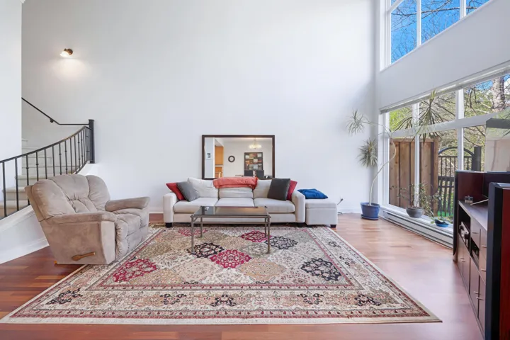 Living room featuring a baseboard heating unit, a towering ceiling, wood finished floors, stairway, and baseboards