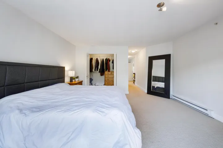 Bedroom with a baseboard radiator, light colored carpet, a walk in closet, and a closet