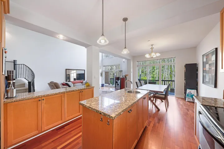 Kitchen featuring a sink, hardwood / wood-style floors, light stone countertops, a chandelier, and a center island with sink