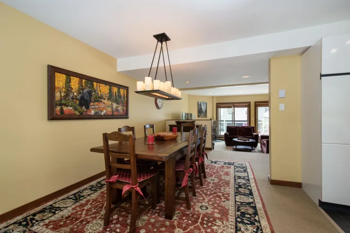 Expansive dining area featuring a rectangular wood dining table with six chairs, an area rug with a floral pattern, and a rectangular chandelier with candle-style lights